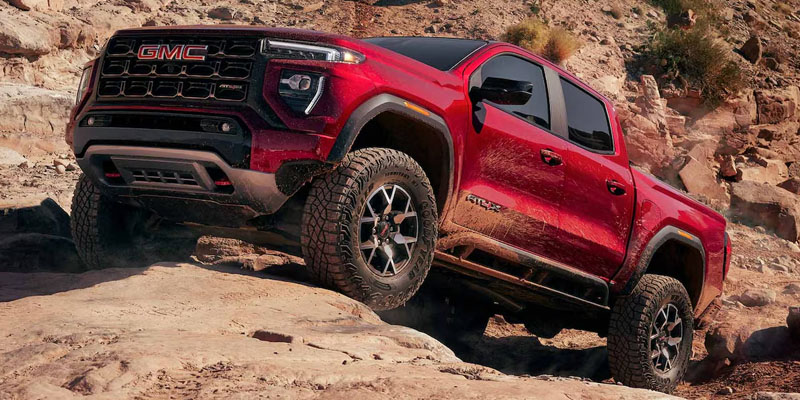 Red 2026 GMC Canyon AT4X off-road truck climbing a rocky desert trail.
